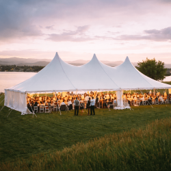 Outdoor wedding tent rental setup in Pittsburgh PA with string lights, round tables, and white folding chairs at evening reception